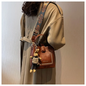 Close-up of brown leather bucket bag with jacquard strap and cute rabbit pendant charm