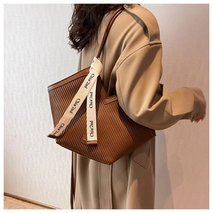 Close-up of brown pleated PU tote bag featuring chic ribbon strap detail on beige trench coat