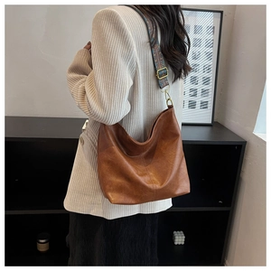 Detail of vintage brown leather bucket bag with wide ethnic embroidered strap and gold hardware