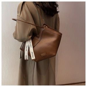 Detail of a brown pleated tote bag featuring a brand metal plaque and decorative strap
