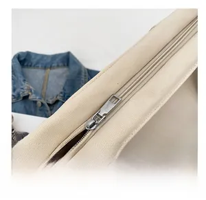 Detailed close-up of the smooth metal zipper on a beige canvas tote bag with denim background