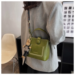 Close-up of olive green bucket bag with textured leather, wide strap, and bunny charm