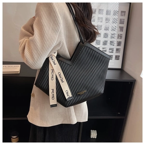 Detail of black pleated faux leather tote bag with stylish V-cut top and ivory ribbon