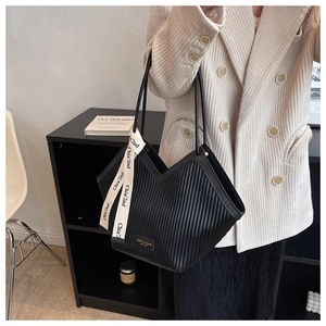 Detail of black pleated tote bag featuring a V-cut edge and branded woven ribbon
