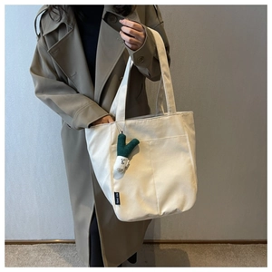 Detail of off-white canvas tote bag featuring an onion doll charm and black text label