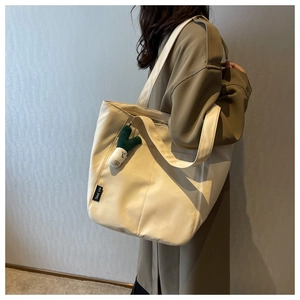 Detail of off-white canvas tote bag featuring a brand woven label and cute plush charm