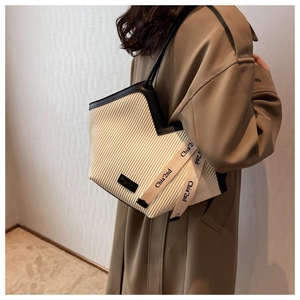 Detail of cream pleated tote bag featuring contrast black straps and silk ribbon ornament