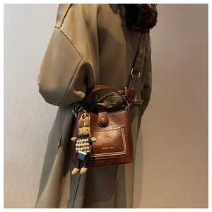 Detail of dark brown leather bucket bag with logo pocket and woven shoulder strap