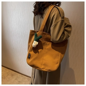 Detail of ginger yellow canvas tote bag with a creative scalloped plush charm on the strap
