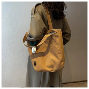 Detail of tan canvas tote bag with side pocket and green plant plush charm accessory