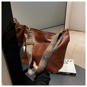 Detail of vintage brown leather bag with colorful ethnic patterned wide strap and bronze hardware