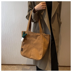 Detail of a brown canvas tote bag with a scalloped pocket and a green scalloped charm