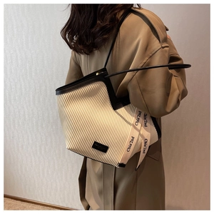 Detail of beige corduroy tote bag showing vertical pleated texture and brand ribbon strap