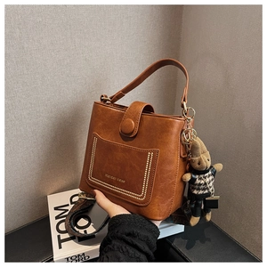 Detail of brown PU leather bucket bag with gold rivets and a mini teddy bear charm