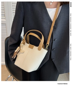 Detail einer beigen Eimer-Handtasche mit khakifarbenen Riemen und Hundeanhänger