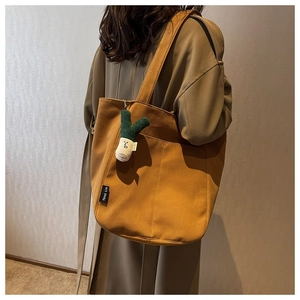 Detail of canvas tote bag with a brown outer pocket and a creative plush leek charm