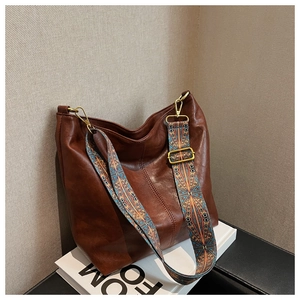 Close-up of vintage brown leather bucket bag with colorful geometric patterned wide strap