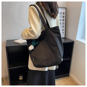 Detail of black canvas tote bag with outer pocket and green leek plush charm pendant