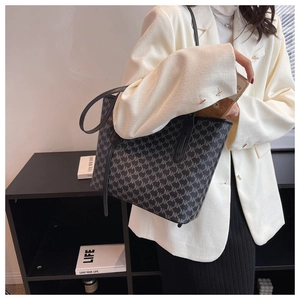 Close-up of charcoal grey tote bag with monogram pattern on a model in a white blazer