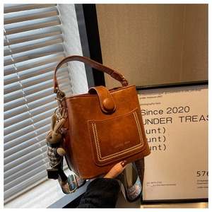 Detail of a brown bucket bag with a patterned wide strap and a cute rabbit charm