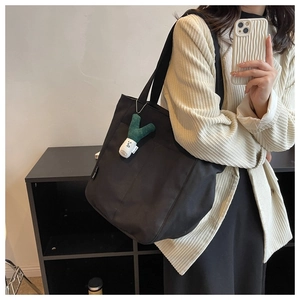 Side view of black canvas tote bag with a quirky green onion plush charm for commuting