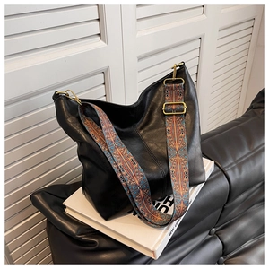 Detail of black leather tote bag with a wide bohemian patterned strap on a white book