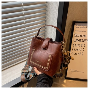 Detail of dark brown leather bucket bag with bohemian strap and cute bear charm