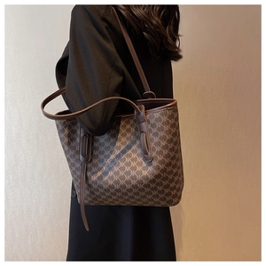 Detail of brown monogram tote bag with NK pattern and slim shoulder straps on model