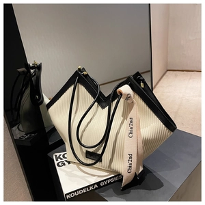 Detail of pleated tote bag with black leather trim, V-shaped cut and decorative ribbon