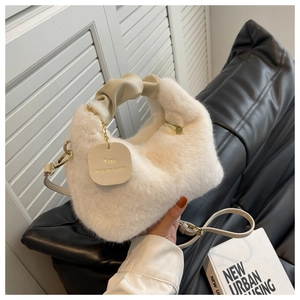 Détail d'un sac en fausse fourrure blanche avec poignée beige et pendentif doré gravé