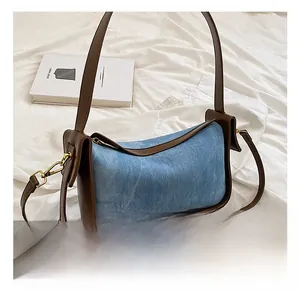 Detail of blue denim bag with brown leather trim and golden lobster clasp on white fabric