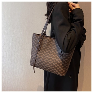 Close-up of a large brown monogram tote bag styled with a professional black blazer