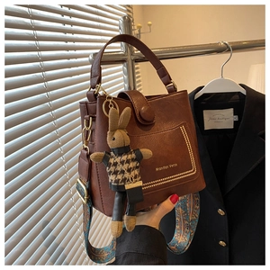 Detail of brown leather bucket bag with gold logo, rivet pocket and bunny charm