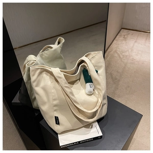 Detail of off-white canvas tote bag texture with brand label and plush charm