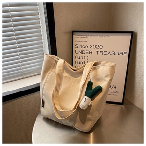 Detail of beige canvas tote bag with green onion plush pendant on a metal table