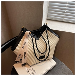 Chic cream pleated PU tote bag with black trim and ribbon on a cozy wooden chair