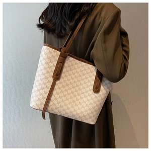 Side view of large tote bag with MK logo print and brown handles on a green blazer model