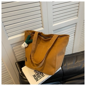 Detail of caramel canvas tote bag with front pocket and green plush charm accessory