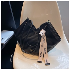 Detail of black pleated PU shoulder bag with decorative ribbon on a minimalist chair