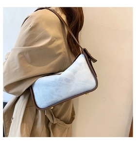 Detail of blue denim shoulder bag with brown leather trim and metal rivets on base
