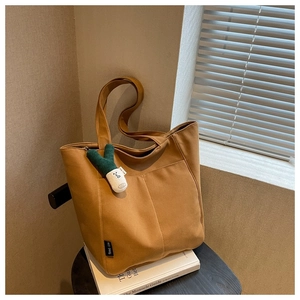 Detail of a brown canvas tote bag featuring structured stitching and a plush charm