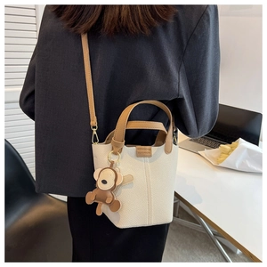 Detail einer cremefarbenen Beuteltasche mit braunen Griffen und einem Affenanhänger