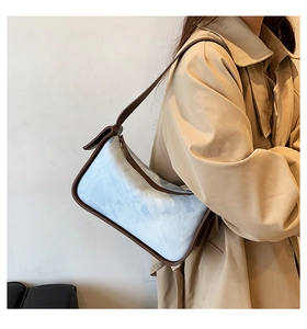 Detail of blue denim shoulder bag with brown leather trim worn with a khaki trench coat