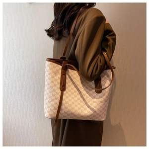 Detail of large tote bag with NK monogram pattern and brown leather straps on model