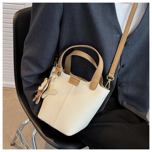Detail einer cremefarbenen Beuteltasche aus Leder mit braunen Griffen und Bärenanhänger