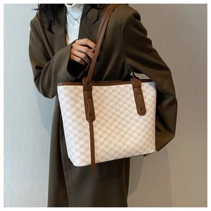 Model wearing a large ivory tote bag with brown leather trim and NK monogram patterns