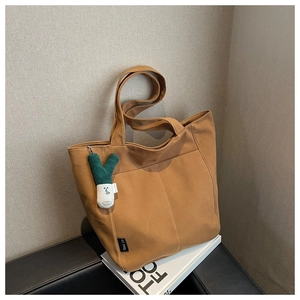 Detail of tan canvas tote bag with dual straps and large front pocket on a white pedestal
