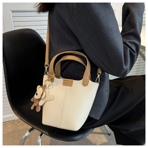 Detail der cremeweißen Beuteltasche mit braunen Griffen und süßem Bären-Schlüsselanhänger