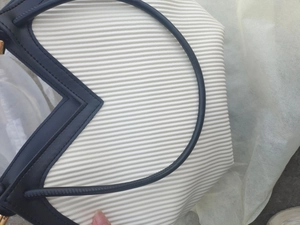 Detail of white pleated tote bag with black contrast trim and V-shaped opening