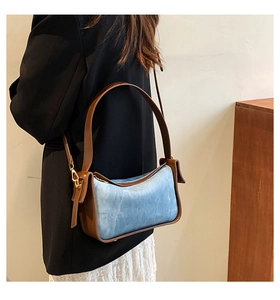 Detail of light blue denim underarm bag with brown leather trim and metal feet on base